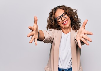 Middle age beautiful businesswoman wearing glasses standing over isolated white background looking at the camera smiling with open arms for hug. Cheerful expression embracing happiness.