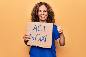 Fototapeta na wymiar Middle age beautiful woman asking for react holding banner with act now message smiling happy and positive, thumb up doing excellent and approval sign