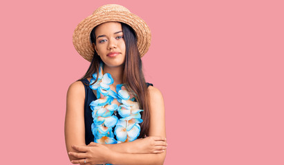 Young beautiful latin girl wearing hawaiian lei and summer hat relaxed with serious expression on face. simple and natural looking at the camera.