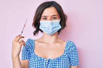 Young beautiful woman wearing medical mask holding syringe thinking attitude and sober expression looking self confident