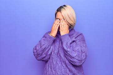 Beautiful blonde plus size woman wearing casual turtleneck sweater over purple background rubbing...