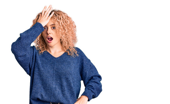 Young blonde woman with curly hair wearing casual winter sweater surprised with hand on head for mistake, remember error. forgot, bad memory concept.