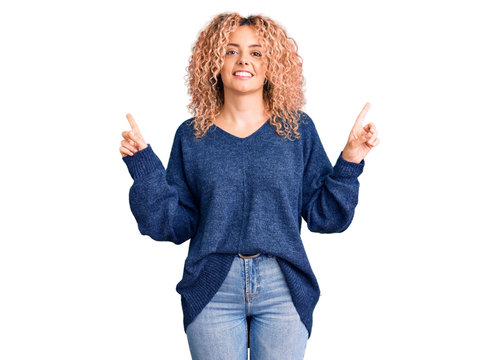 Young blonde woman with curly hair wearing casual winter sweater smiling confident pointing with fingers to different directions. copy space for advertisement