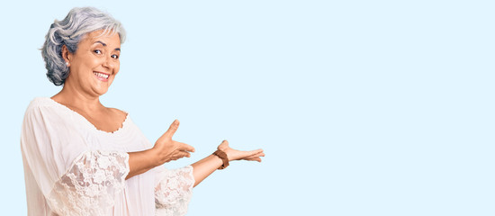 Senior woman with gray hair wearing bohemian style inviting to enter smiling natural with open hand
