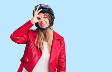 Young beautiful woman wearing motorcycle helmet smiling happy doing ok sign with hand on eye looking through fingers