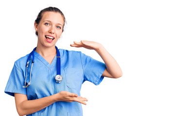 Young beautiful blonde woman wearing doctor uniform and stethoscope gesturing with hands showing big and large size sign, measure symbol. smiling looking at the camera. measuring concept.