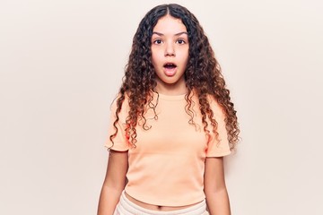 Beautiful kid girl with curly hair wearing casual clothes scared and amazed with open mouth for surprise, disbelief face