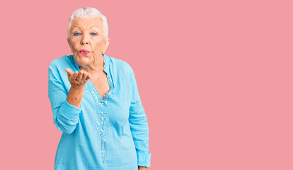 Senior beautiful woman with blue eyes and grey hair wearing summer dress looking at the camera blowing a kiss with hand on air being lovely and sexy. love expression.