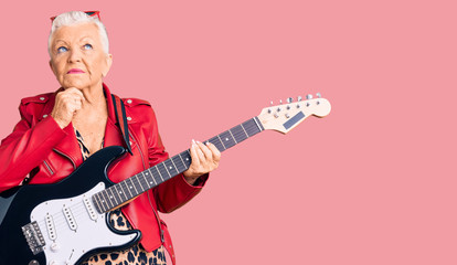 Fototapeta premium Senior beautiful woman with blue eyes and grey hair wearing a modern look playing electric guitar with hand on chin thinking about question, pensive expression. smiling with thoughtful face. doubt