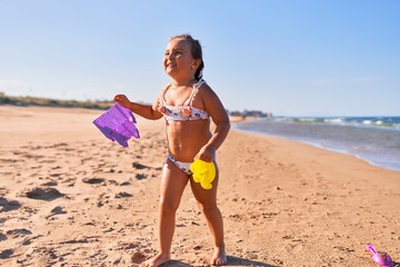 Adorable blonde child wearing bikini. Building sand castle using bucket and shovel at the beach