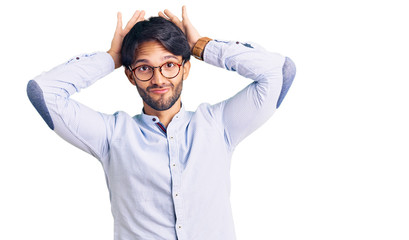 Handsome hispanic man wearing business shirt and glasses doing bunny ears gesture with hands palms...