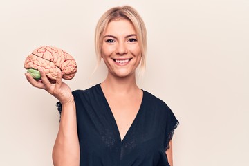 Young beautiful blonde woman asking for care memory holding brain over white background looking...