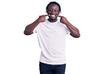 Young african american man with braids wearing casual white tshirt smiling cheerful showing and pointing with fingers teeth and mouth. dental health concept.