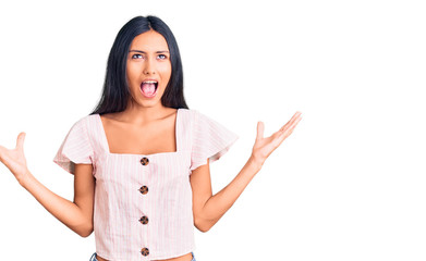 Young beautiful latin girl wearing casual clothes crazy and mad shouting and yelling with aggressive expression and arms raised. frustration concept.