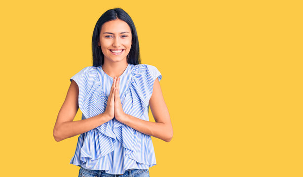 Young beautiful latin girl wearing casual clothes praying with hands together asking for forgiveness smiling confident.