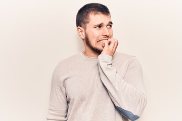 Young handsome man wearing casual sweater looking stressed and nervous with hands on mouth biting nails. anxiety problem.