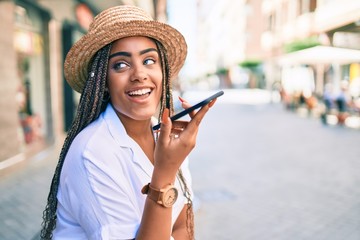 Young african american woman with braids smiling happy using smartphone outdoors on a sunny day of summer