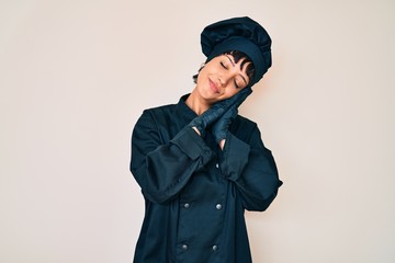 Beautiful brunettte woman wearing professional cook uniform sleeping tired dreaming and posing with hands together while smiling with closed eyes.