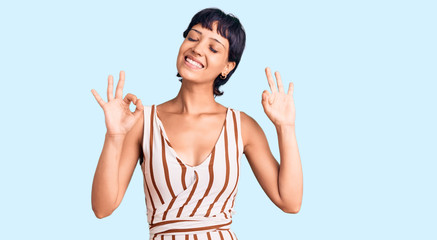 Young brunette woman with short hair wearing summer outfit relax and smiling with eyes closed doing meditation gesture with fingers. yoga concept.