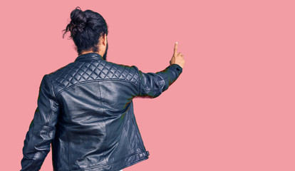 Young arab man wearing casual leather jacket posing backwards pointing ahead with finger hand