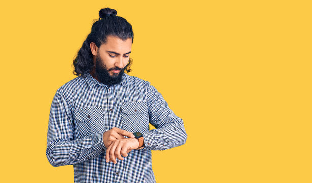 Young arab man wearing casual clothes checking the time on wrist watch, relaxed and confident