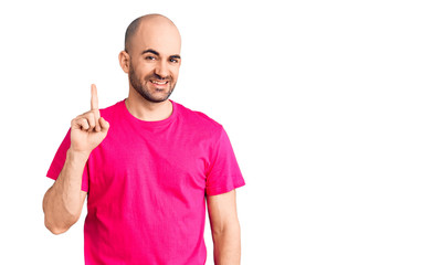 Young handsome man wearing casual t shirt showing and pointing up with finger number one while smiling confident and happy.