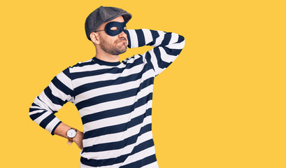 Young handsome man wearing burglar mask suffering of neck ache injury, touching neck with hand, muscular pain
