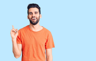 Young handsome man with beard wearing casual t-shirt with a big smile on face, pointing with hand finger to the side looking at the camera.