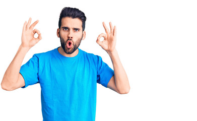 Fototapeta premium Young handsome man with beard wearing casual t-shirt looking surprised and shocked doing ok approval symbol with fingers. crazy expression