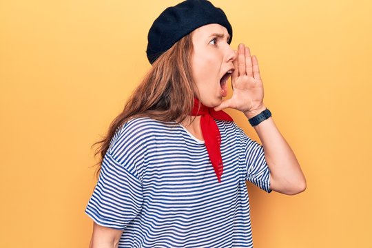 Young beautiful blonde woman wearing french fashion style with scarf and beret shouting and screaming loud to side with hand on mouth. communication concept.