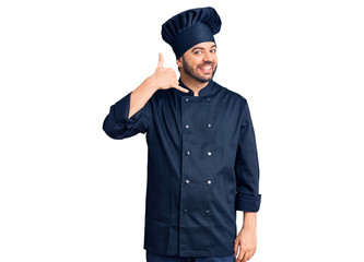 Young hispanic man wearing cooker uniform smiling doing phone gesture with hand and fingers like talking on the telephone. communicating concepts.