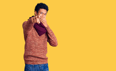 Young african american man wearing casual winter sweater and scarf laughing at you, pointing finger to the camera with hand over mouth, shame expression