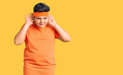 Little boy kid wearing sportswear trying to hear both hands on ear gesture, curious for gossip. hearing problem, deaf