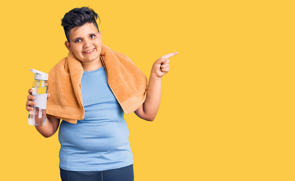 Little boy kid wearing sportswear drinking bottle of water smiling happy pointing with hand and finger to the side