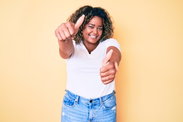 Young african american plus size woman wearing casual white tshirt approving doing positive gesture with hand, thumbs up smiling and happy for success. winner gesture.