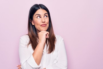 Young beautiful brunette woman wearing elegant shirt standing over isolated pink background...