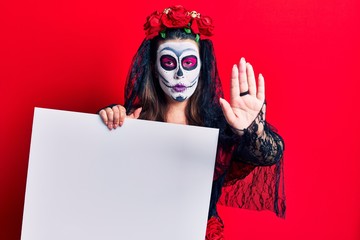 Young woman wearing day of the dead costume holding blank empty banner with open hand doing stop sign with serious and confident expression, defense gesture