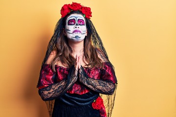 Young woman wearing day of the dead costume over yellow begging and praying with hands together with hope expression on face very emotional and worried. begging.