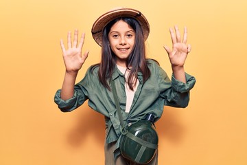 Beautiful child girl wearing explorer hat showing and pointing up with fingers number nine while smiling confident and happy.