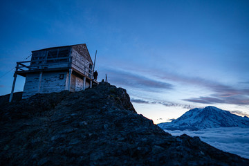 Fire lookout on top of mountain with Mount Rainier in the background during sunrise