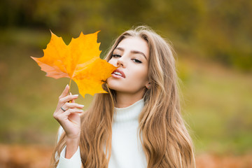 Autumn beauty. Woman fashion wodel with fall maple leaf outdoors. Young woman enjoying warm weather. People on yellow foliage background.