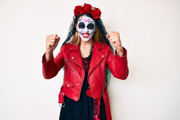 Woman wearing day of the dead costume over white angry and mad raising fists frustrated and furious while shouting with anger. rage and aggressive concept.