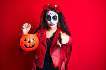 Woman wearing day of the dead costume holding pumpkin pointing with finger to the camera and to you, confident gesture looking serious