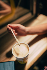 A female hand holding a stick over a latte paper mug