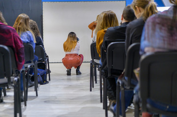 Obraz premium The girl in the aisle between the chairs. Taking pictures with the camera. View from the back. Concept - seminar, workshop. Selective focus.