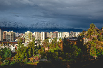 Fototapeta na wymiar Amazing cloudy sky over Santiago skyline, Santa Lucía hill and the snowed The Andes Mountains, and a beautiful sunlight over the city, Chile