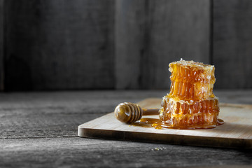 Pieces of fresh honeycomb with honey and wooden stick on old wooden background. Craft concept