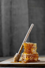 Pieces of fresh honeycomb with honey and wooden stick on old wooden background. Craft concept