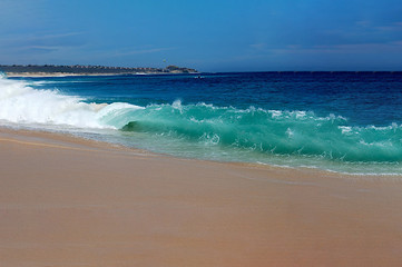 white and turquoise waves crashing on a sandy beach from a deep blue ocean with a bright blue summer sky