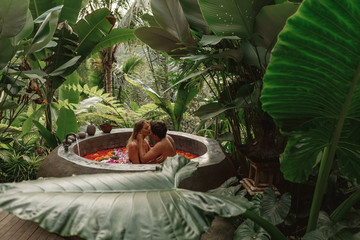 Beautiful couple resting in hotel spa. Woman and man relaxing in bath with tropical flowers outdoor...
